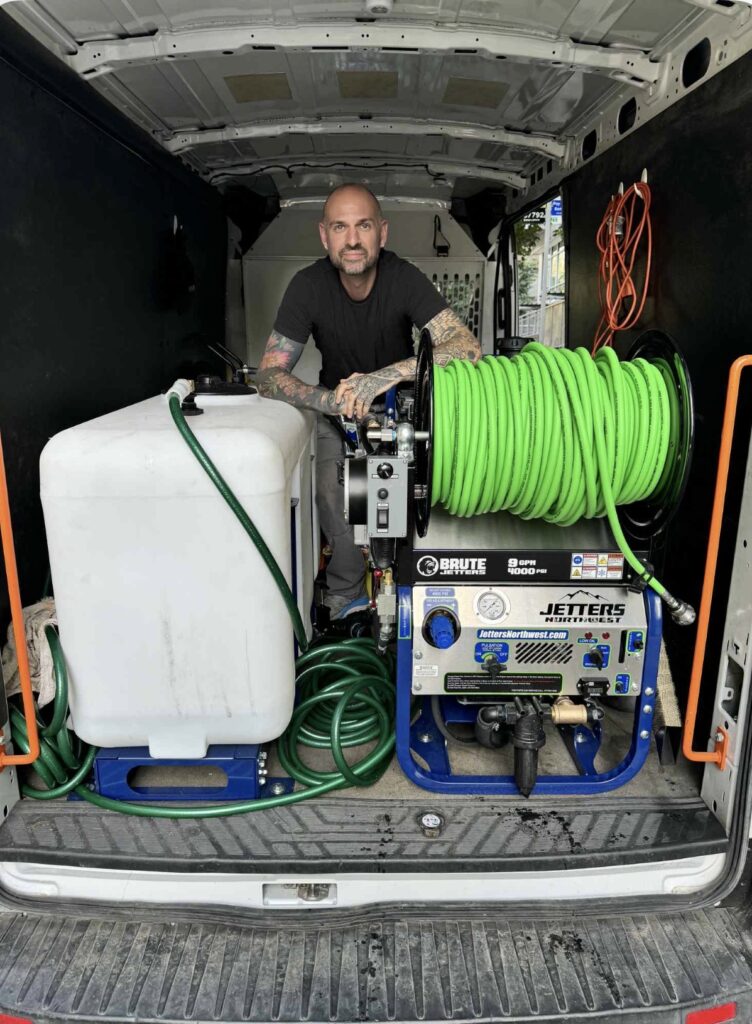 Shane Caldwell of The Drain Authority in the back of his van beside the jetter and hose reel