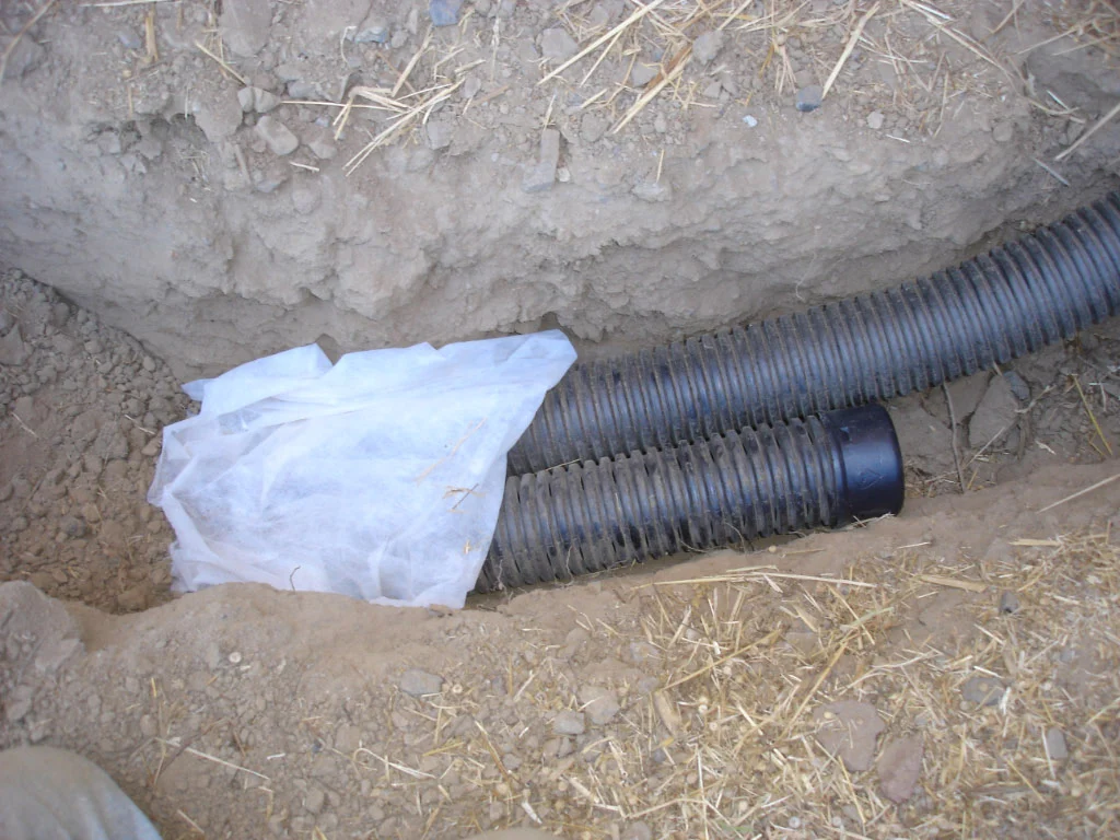 Perforated drain pipe wrapped in filter fabric laid in a dug trench for a French drain