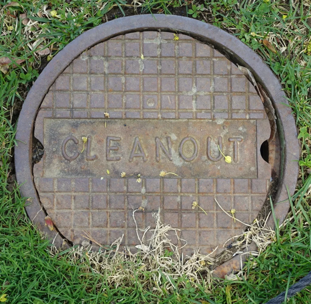 Cast iron sewer cleanout cover stamped CLEANOUT set in a grassy lawn